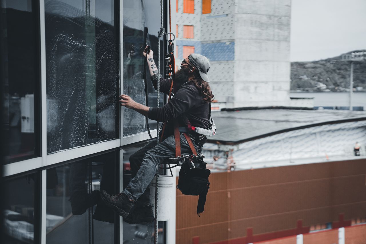 Un homme nettoie les vitres d’un gratte-ciel avec un harnais, illustrant le travail en hauteur en milieu urbain.